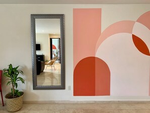 A hallway with a large mirror, a potted plant, and a wall with abstract art.