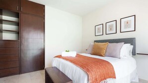 A bedroom with a bed, a bench, a wardrobe, and three framed pictures on the wall.