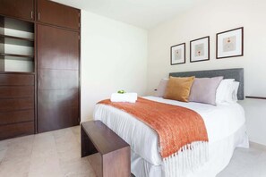 A bedroom with a bed, a bench, a wardrobe, and three framed pictures on the wall.