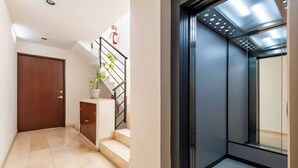 A hallway with a wooden door, a staircase with a handrail, a potted plant, and a fire extinguisher.