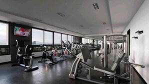A gym with various exercise machines, a television, and large windows offering a city view.