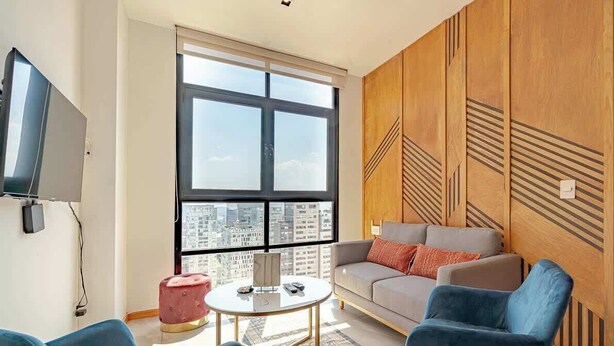 A modern living room with a large window, a sofa, two armchairs, and a small round table.