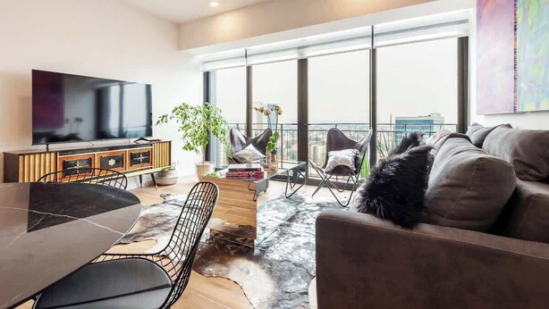 A modern living room with a large TV, comfortable seating, a dining area, and a balcony with large windows. - Stunning High-Rise Panoramic Apartment Polanco 3BD (Ciudad de México)