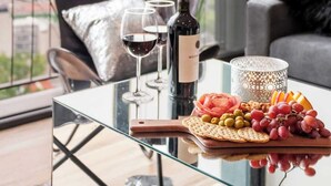A modern living room with a glass table, a wine bottle, glasses, and a fruit platter. - Stunning High-Rise Panoramic Apartment Polanco 3BD (Ciudad de México)