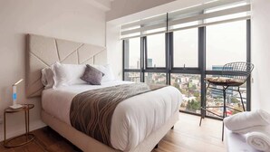 A modern bedroom with a large bed, a view of the city through floor-to-ceiling windows, and a small side table with a lamp. - Stunning High-Rise Panoramic Apartment Polanco 3BD (Ciudad de México)