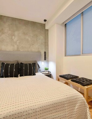 Une chambre moderne avec un grand lit, une table de chevet avec une lampe et une fenêtre avec des stores.