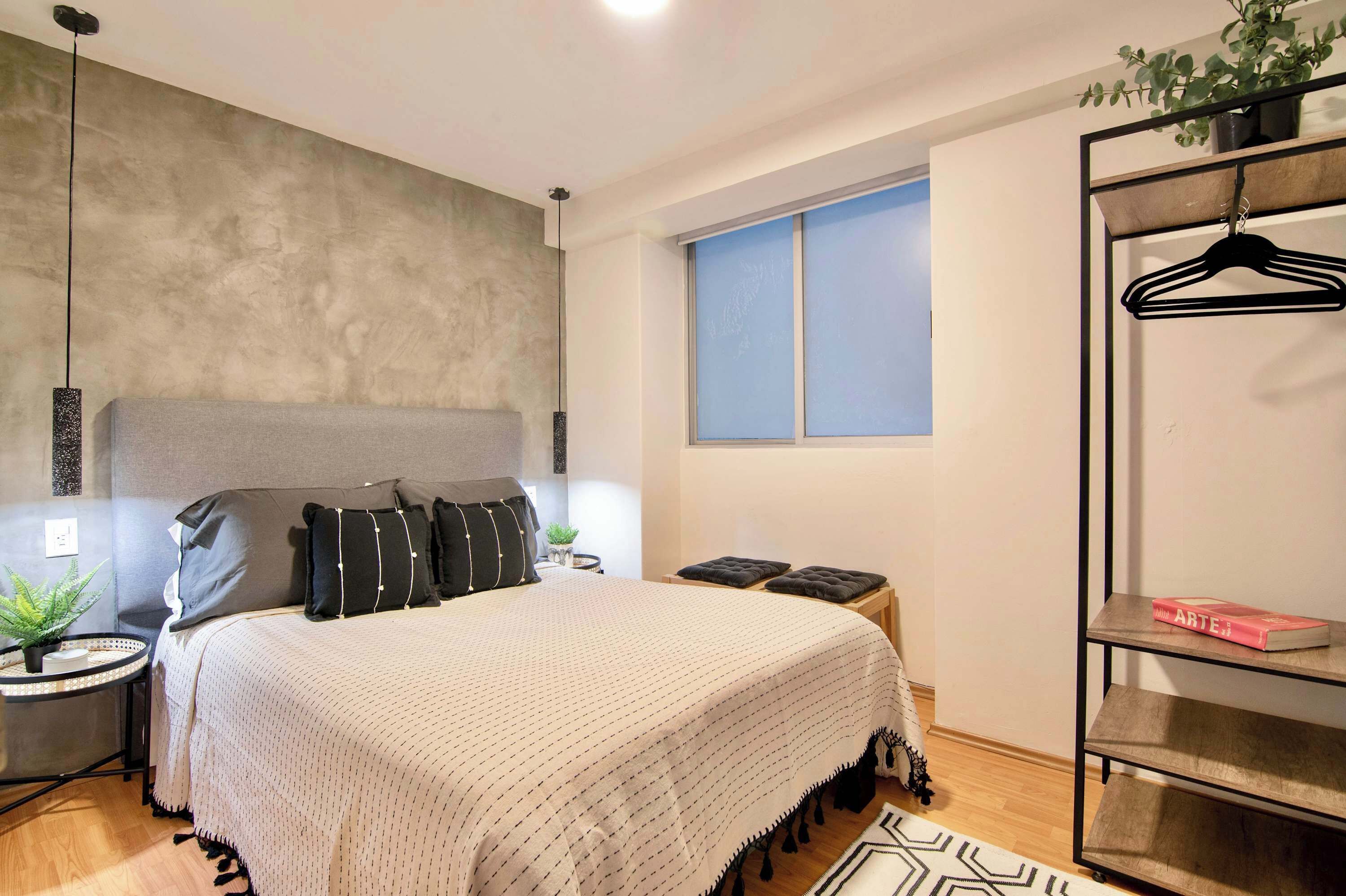 A bedroom with a bed, bedside tables, a hanging plant, a window, and a wardrobe.