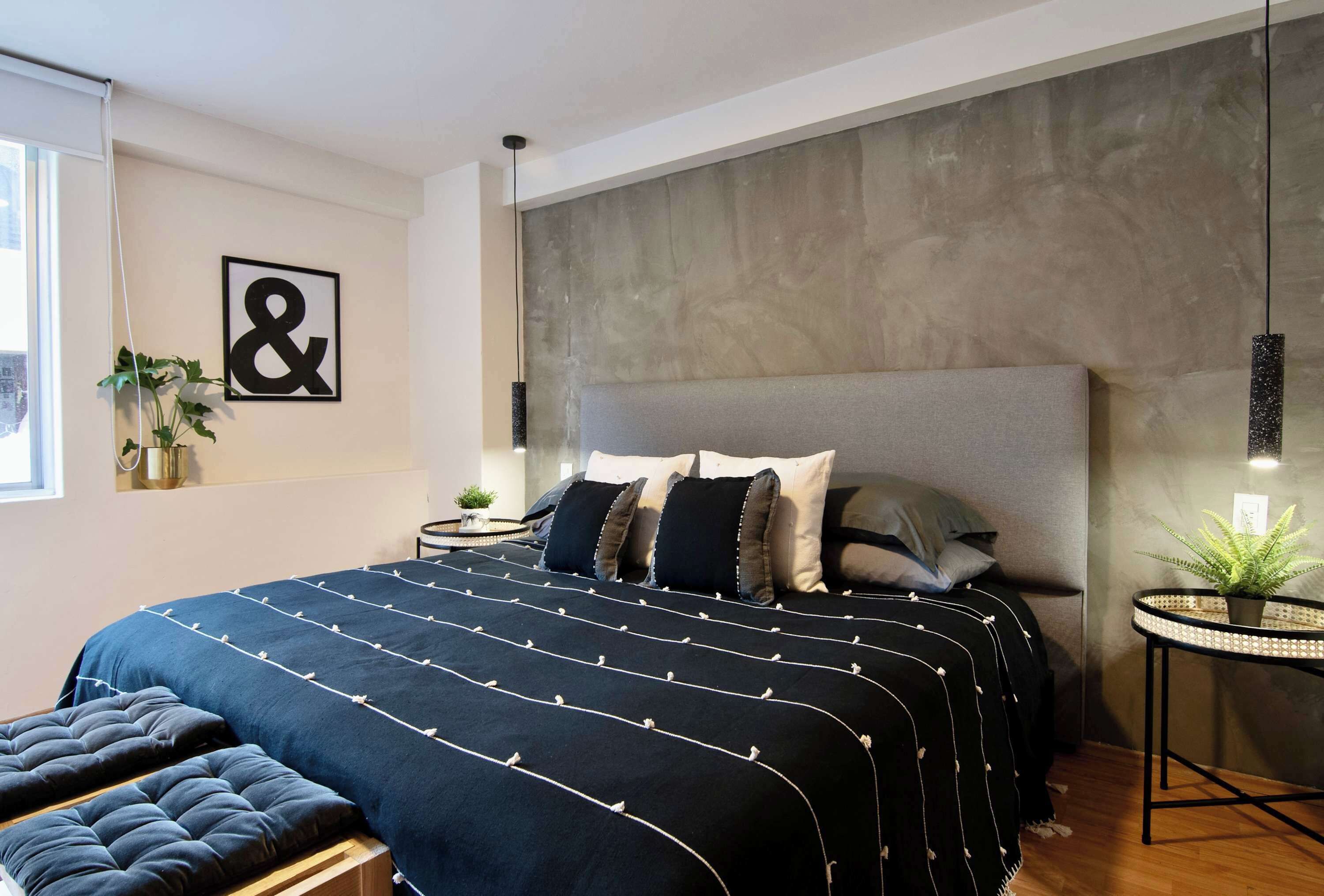 A modern bedroom with a large bed, a headboard, bedside tables, and a small round table with a plant.