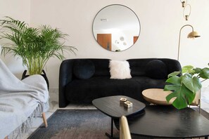 Un salon avec un canapé noir, une table basse ronde, un miroir au mur et une plante en pot.