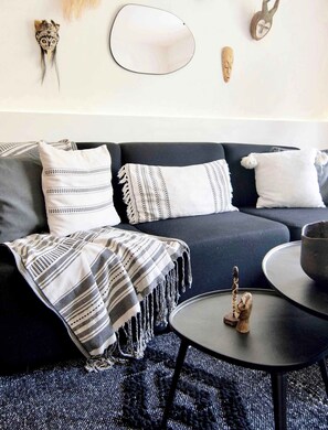 Un salon moderne avec un canapé foncé, des coussins à motifs, un plaid, une petite table agrémentée d’un objet décoratif et des éléments décoratifs fixés au mur.