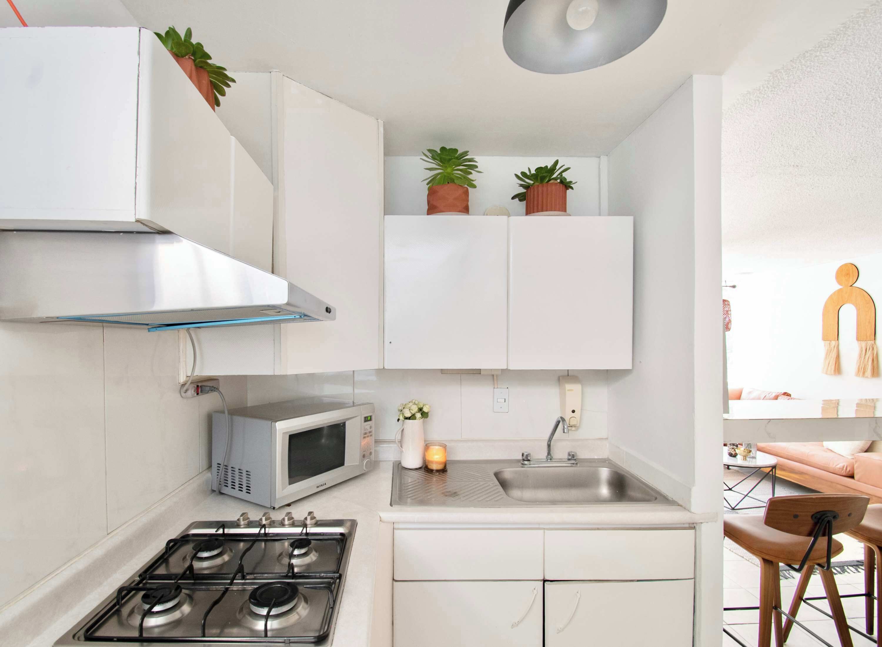 Une cuisine de taille réduite, équipée d’une cuisinière à gaz, d’un four à micro-ondes et de meubles blancs.