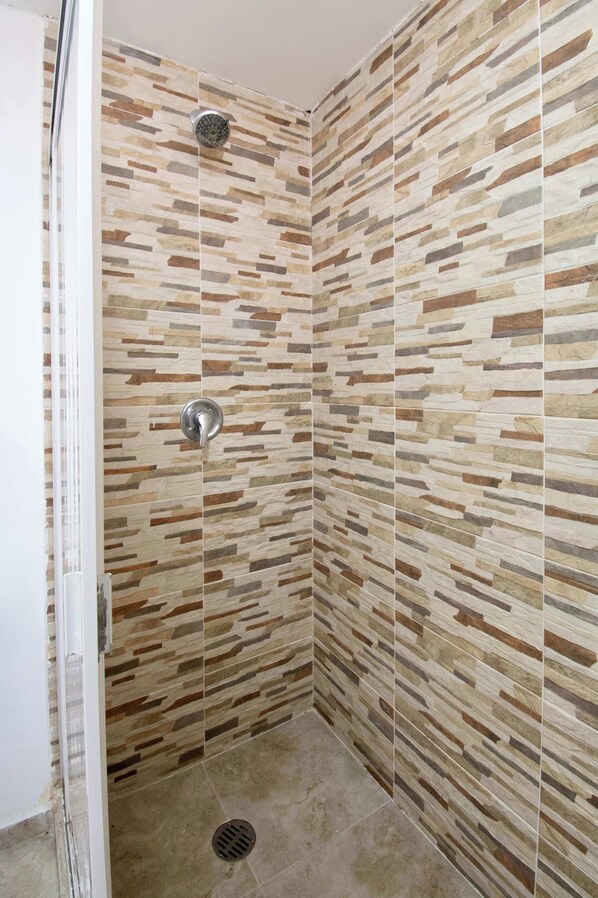 A shower with a stone-patterned wall, a showerhead, and a drain.