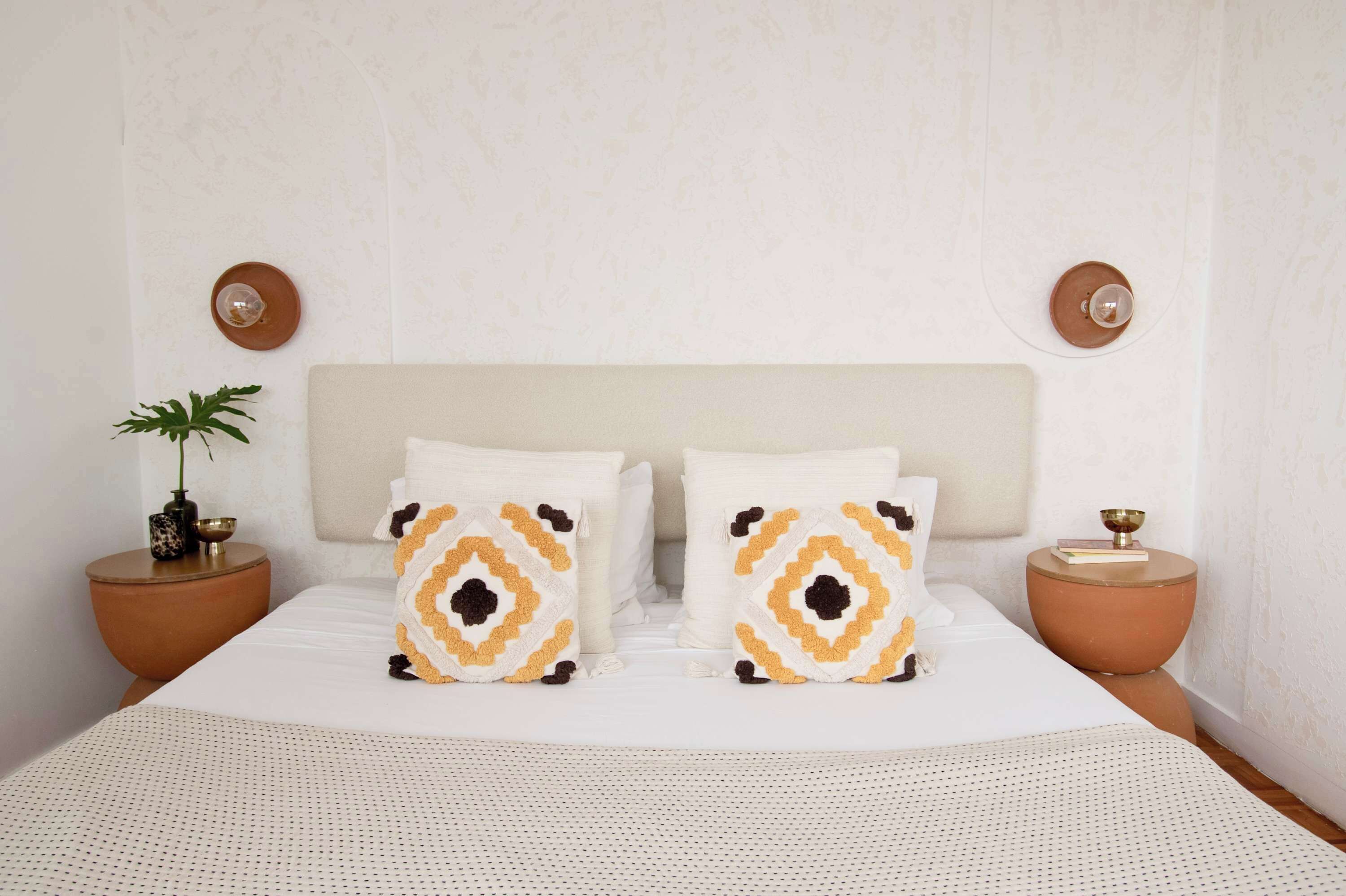 A neatly made bed with patterned pillows, a potted plant, and two bedside tables with decorative items.