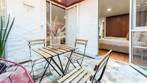 Een terras met een houten tafel en stoelen, een plant in pot en een schuifdeur naar een slaapkamer.