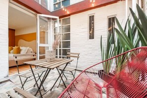 Une pièce avec une table et des chaises en bois, une chaise rouge, un mur en briques blanches et une fenêtre.