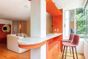 Una cocina moderna con una encimera curva, dos taburetes de bar y vistas al exterior con vegetación.