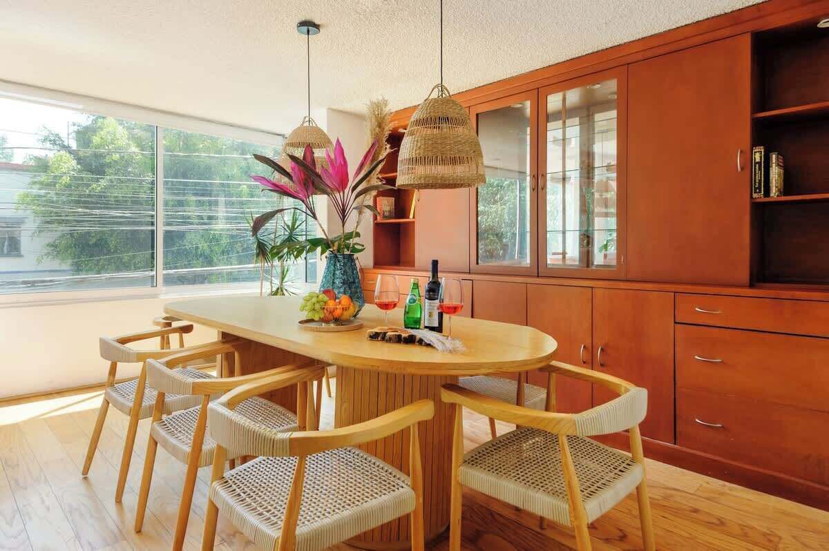 Een moderne keuken met een ronde houten tafel, rieten stoelen en een groot raam.