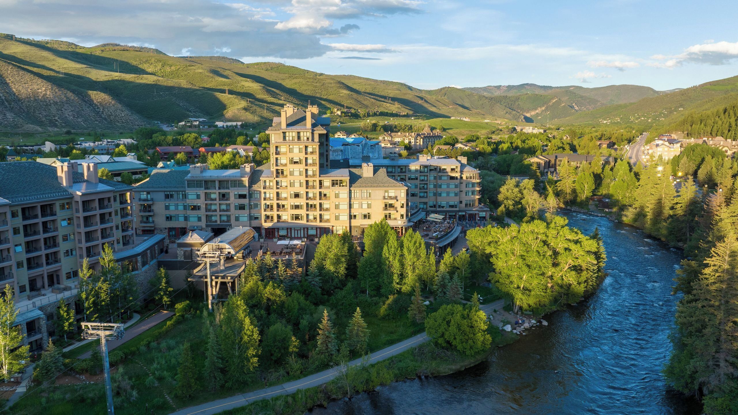 Un hôtel composé de plusieurs bâtiments, situé au bord d’une rivière et entouré de verdure.