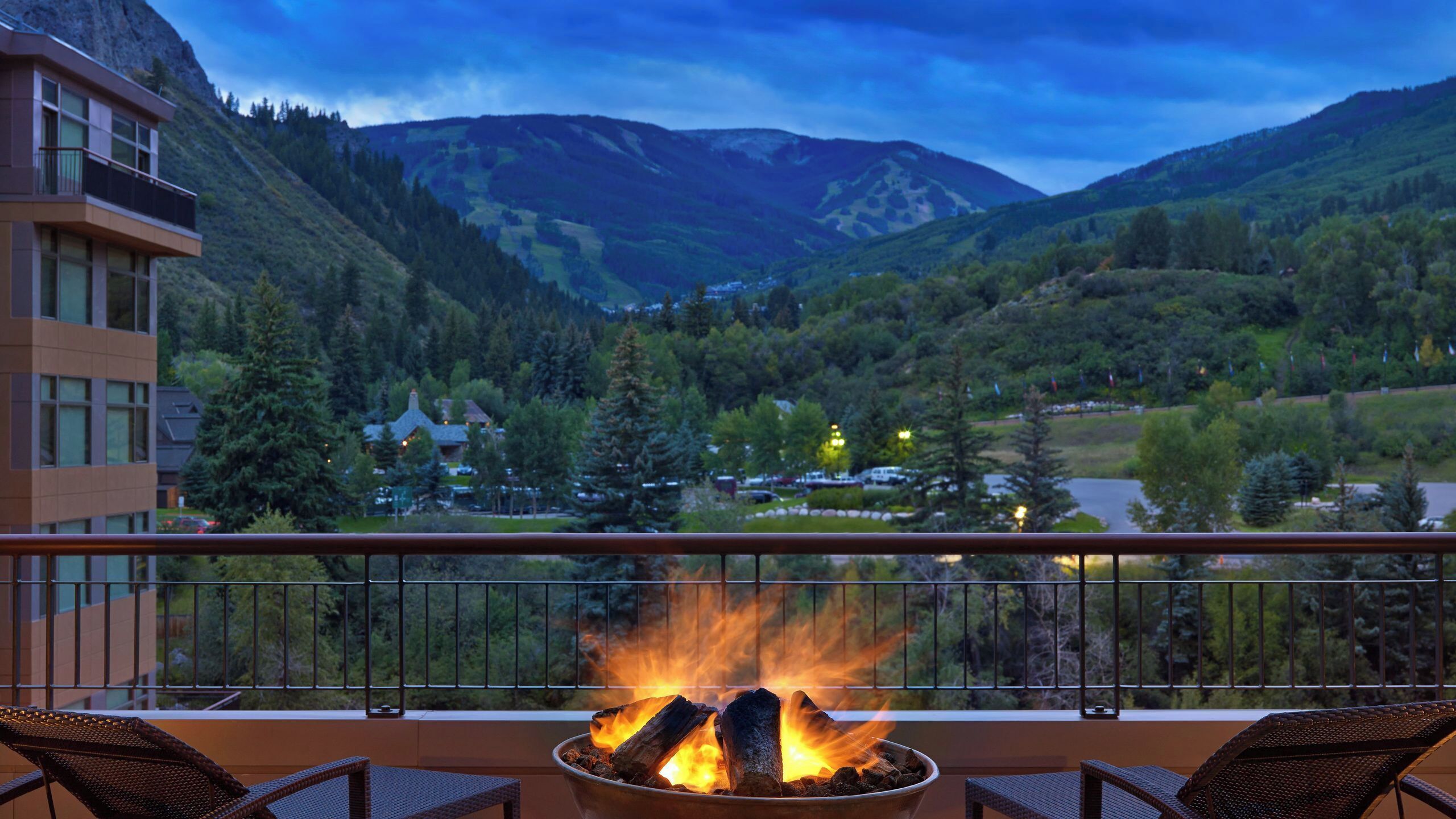 A balcony with a fire pit, overlooking a mountainous landscape with buildings.
