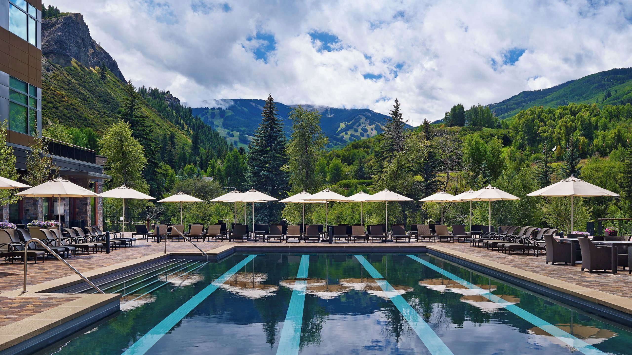 A pool area with lounge chairs and umbrellas, surrounded by mountains and trees.