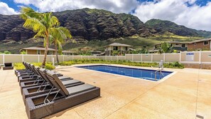 Un área de piscina con sillas de descanso, piscina y un paisaje montañoso de fondo.