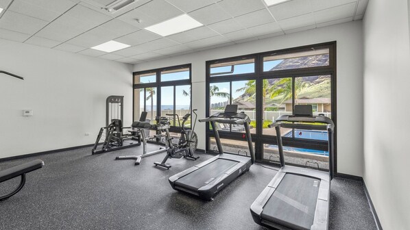 A gym with exercise equipment, large windows, and a view of a pool. - Pakele Oahu by Avantstay 5 Min to Makaha Beach (Waianae)