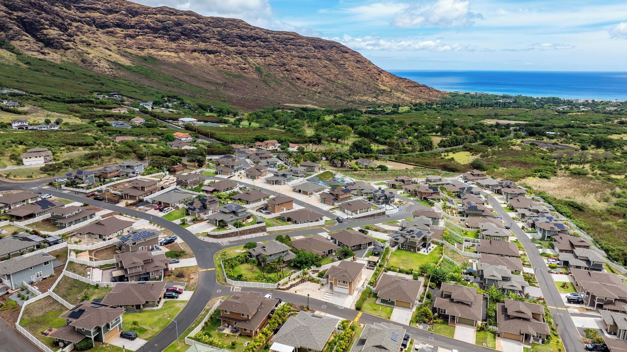 A residential area with houses arranged in a grid pattern, surrounded by greenery and a mountain in the background.