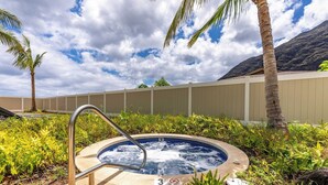 Een hottub omringd door groen en palmbomen, met een bewolkte lucht en bergen op de achtergrond.
