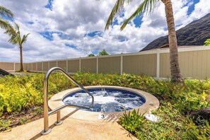 Un jacuzzi rodeado de follaje y palmeras, con un cielo nublado y montañas al fondo.