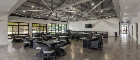 A spacious indoor area with high ceilings, multiple tables and chairs, and large windows allowing natural light.