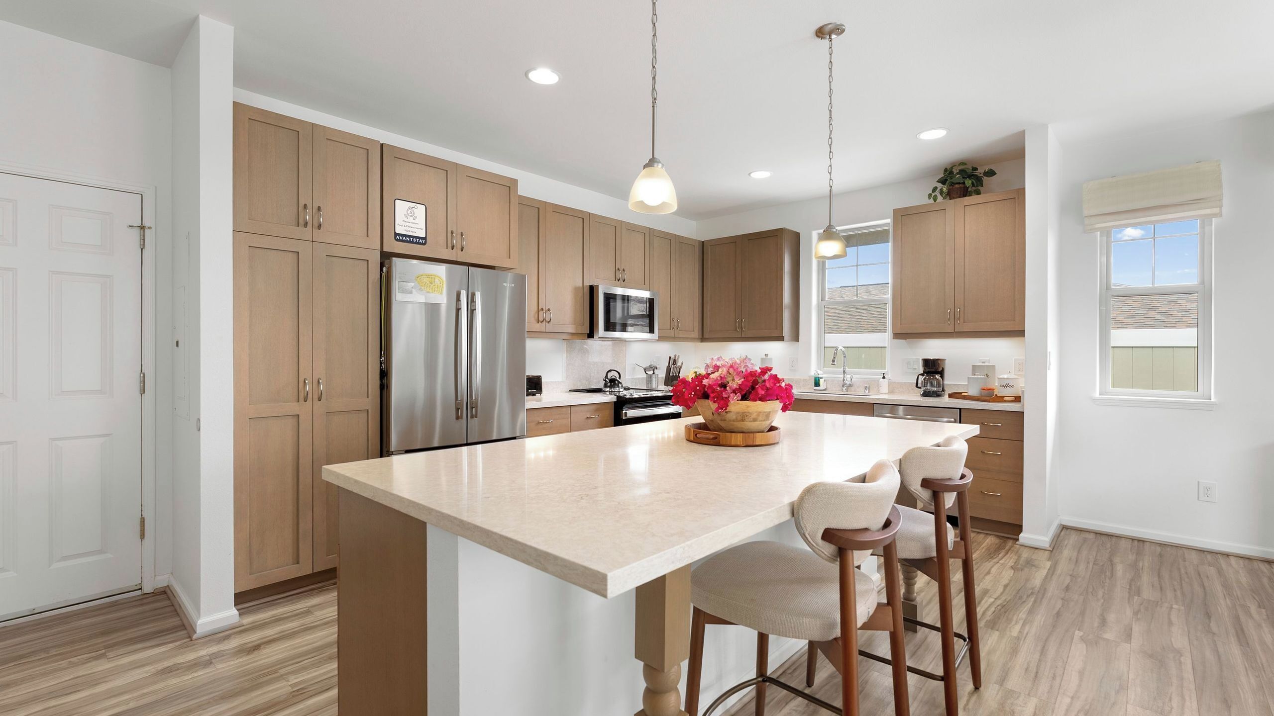 A modern kitchen with wooden cabinets, stainless steel appliances, a large island with bar stools, and pendant lighting.