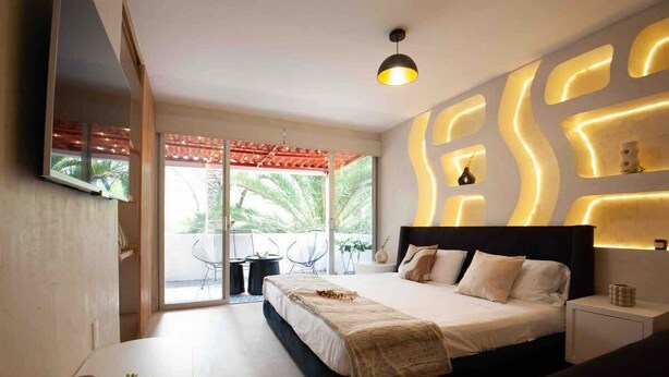Ein modernes Schlafzimmer mit einem großen Bett, einem an der Wand montierten Fernseher und einem Balkon mit Gartenmöbeln.