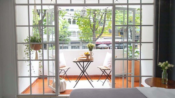 A room with a large sliding glass door leading to an outdoor balcony. The balcony has a table with chairs, a hanging plant, and a vase with flowers. - KOKU! Best location in Polanco 10 guests (Ciudad de México)