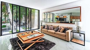 A modern living room with a sofa, a coffee table, and a large window overlooking a garden. - Stunning modern villa with pool & beach access (Playa del Carmen)