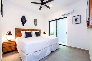 Ein Schlafzimmer mit einem großen Bett, einem Holzkopfende, Nachttischlampen, einem Deckenventilator und einer Glastür zum Balkon.