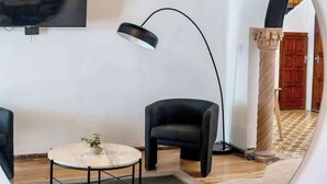 Un intérieur moderne avec un grand miroir rond qui reflète une pièce. On aperçoit une table ronde avec une seule chaise, ainsi qu’un lampadaire noir et un fauteuil noir.
