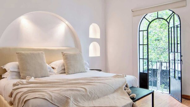 Une chambre avec un grand lit, une petite table et une vue sur la verdure par la fenêtre.