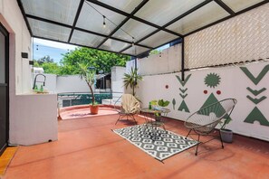 A covered patio with a patterned rug, two chairs, a small table, and potted plants.