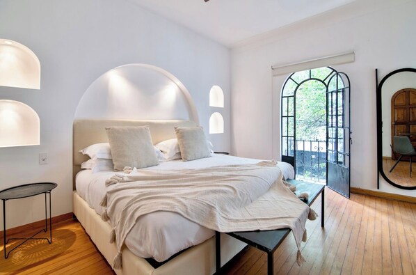 A modern bedroom with a large bed, a bench, and a view of the outdoors through a window.