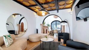 Un salon moderne avec un canapé, un fauteuil et une table basse ronde. On y trouve une cheminée, un coin repas à l’arrière-plan et une grande fenêtre offrant une belle vue.
