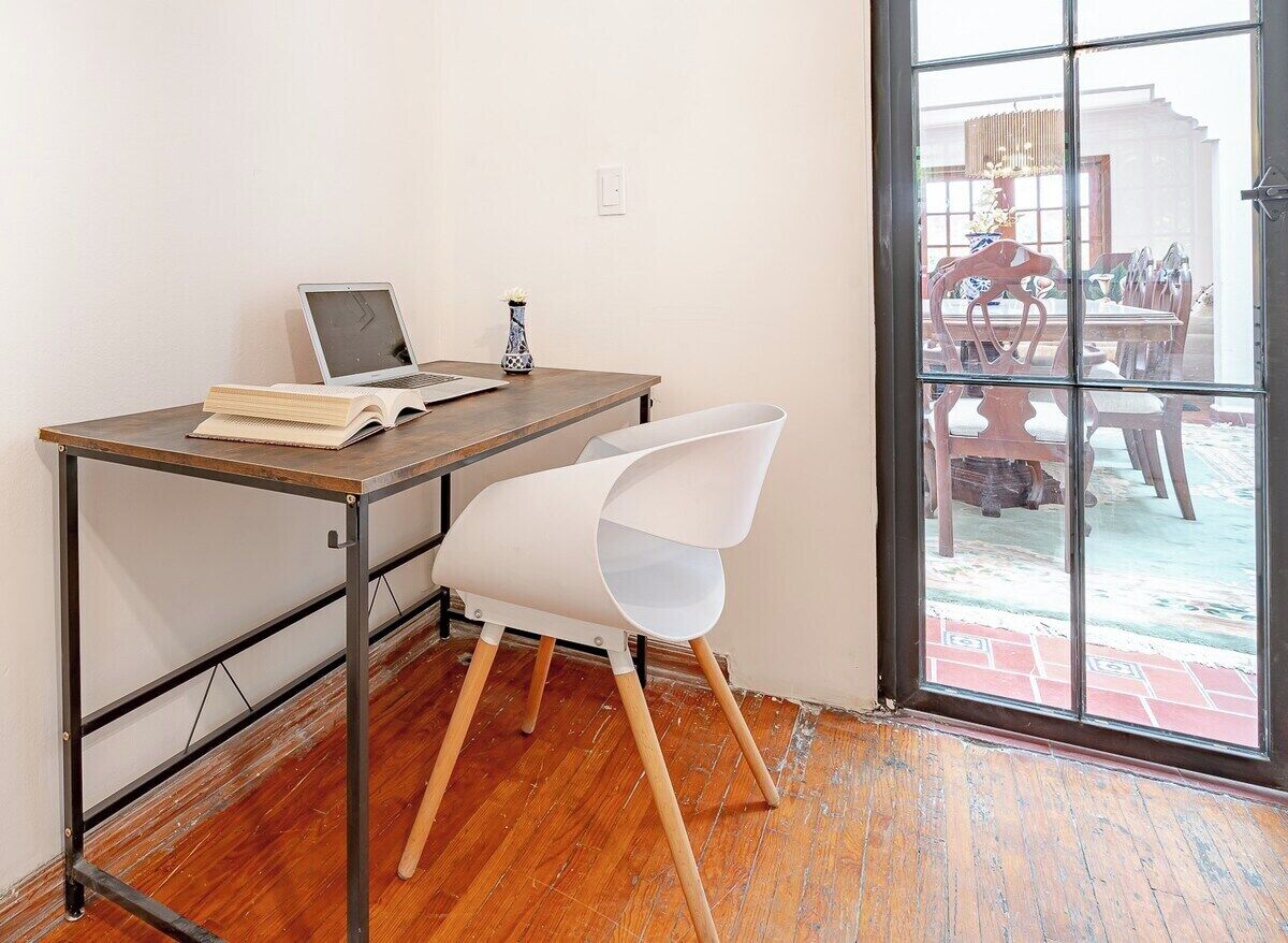 A room with a wooden desk, a laptop, an open book, and a white chair.