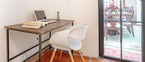 A room with a wooden desk, a laptop, an open book, and a white chair.