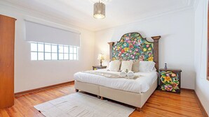 Une chambre à coucher avec un grand lit, une fenêtre, un plancher en bois et une tête de lit décorative.