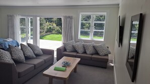 Una sala de estar moderna con dos sofás, una mesa de centro, una cama y ventanas amplias que dan a un jardín.