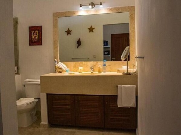A bathroom with a large mirror, a sink, a toilet, and a vanity with cabinets. - Casa Roca Chaac - Whole House (Isla Mujeres)
