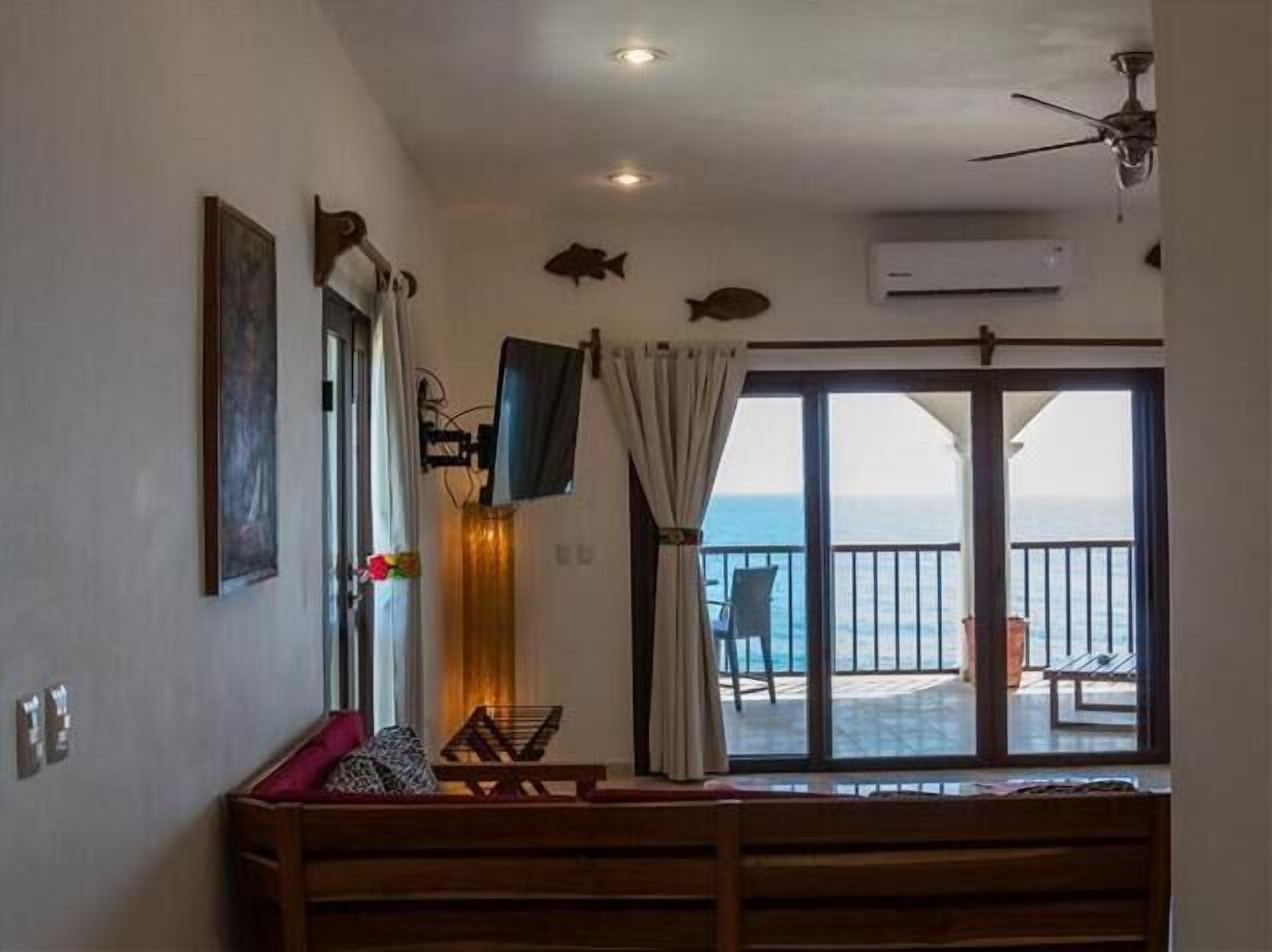 A room with a large sliding glass door to the balcony, a ceiling fan, a mounted TV, and a framed picture on the wall.