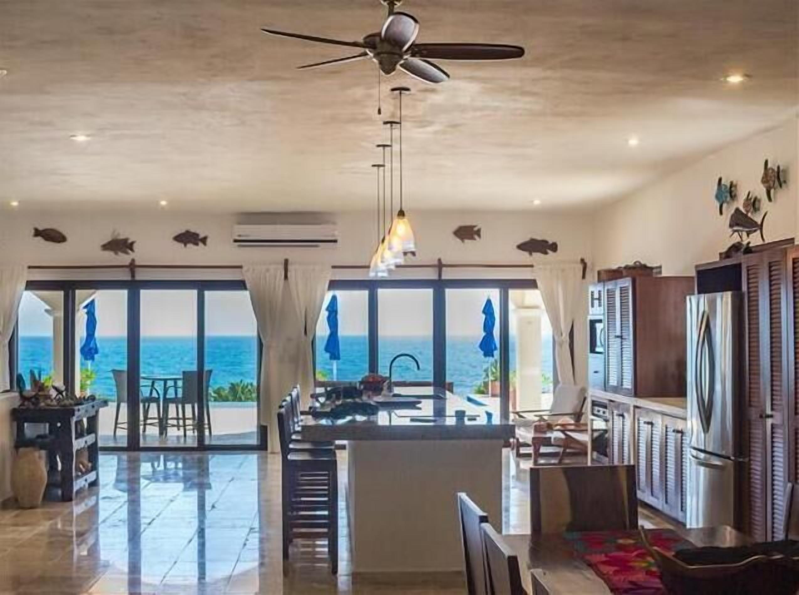 A spacious kitchen with a view of the ocean, a ceiling fan, and a dining area with a view.
