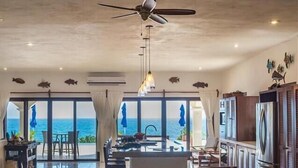 A spacious kitchen with a view of the ocean, a ceiling fan, and a dining area with a view. - Casa Roca Chaac - Whole House (Isla Mujeres)
