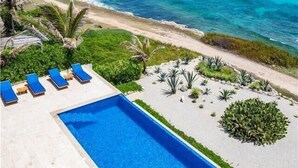 A pool with blue water, surrounded by a sandy area with plants and a beach in the background. - Casa Roca Chaac - Whole House (Isla Mujeres)