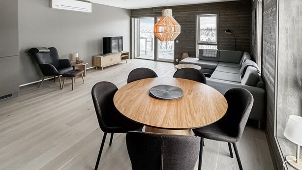 A modern living room with a round wooden dining table, black chairs, a sofa, and a television. - Awesome apartment in Geilo with sauna (Geilo)